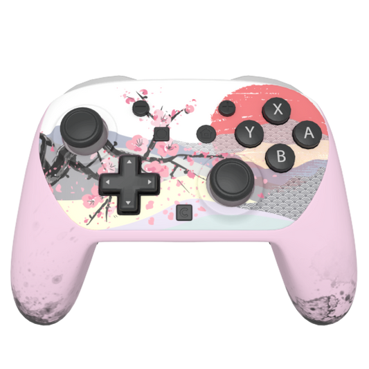A pink and white wireless game controller decorated with a cherry blossom and landscape print, featuring black joysticks, buttons, and a directional pad on a white background.