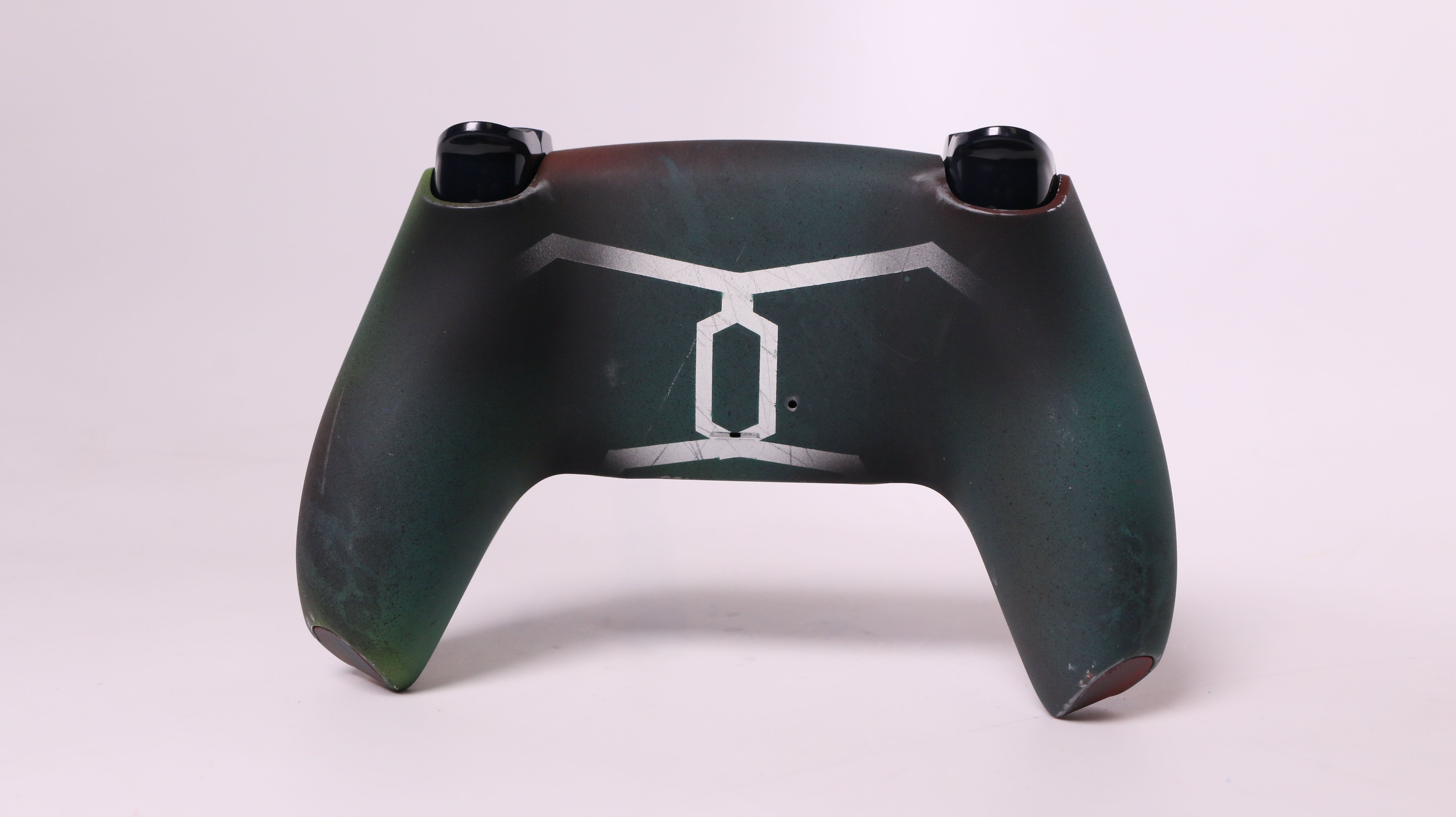 A custom-designed gaming controller shell with a dark green and black textured finish, featuring a white stylized geometric logo on the front, set against a plain light background.