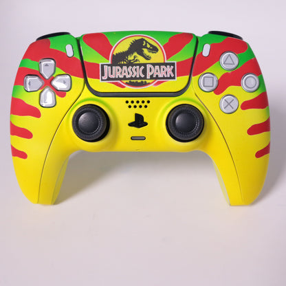 custom-airbrush-painted-dinosaur-theme-ps5-controller-Dino DNA-jeep-Sam Neil-red-yellow-green-TRex A custom PlayStation-style game controller featuring a theme, with a bright yellow body, red and green camouflage patterns, and the  logo on the top center.